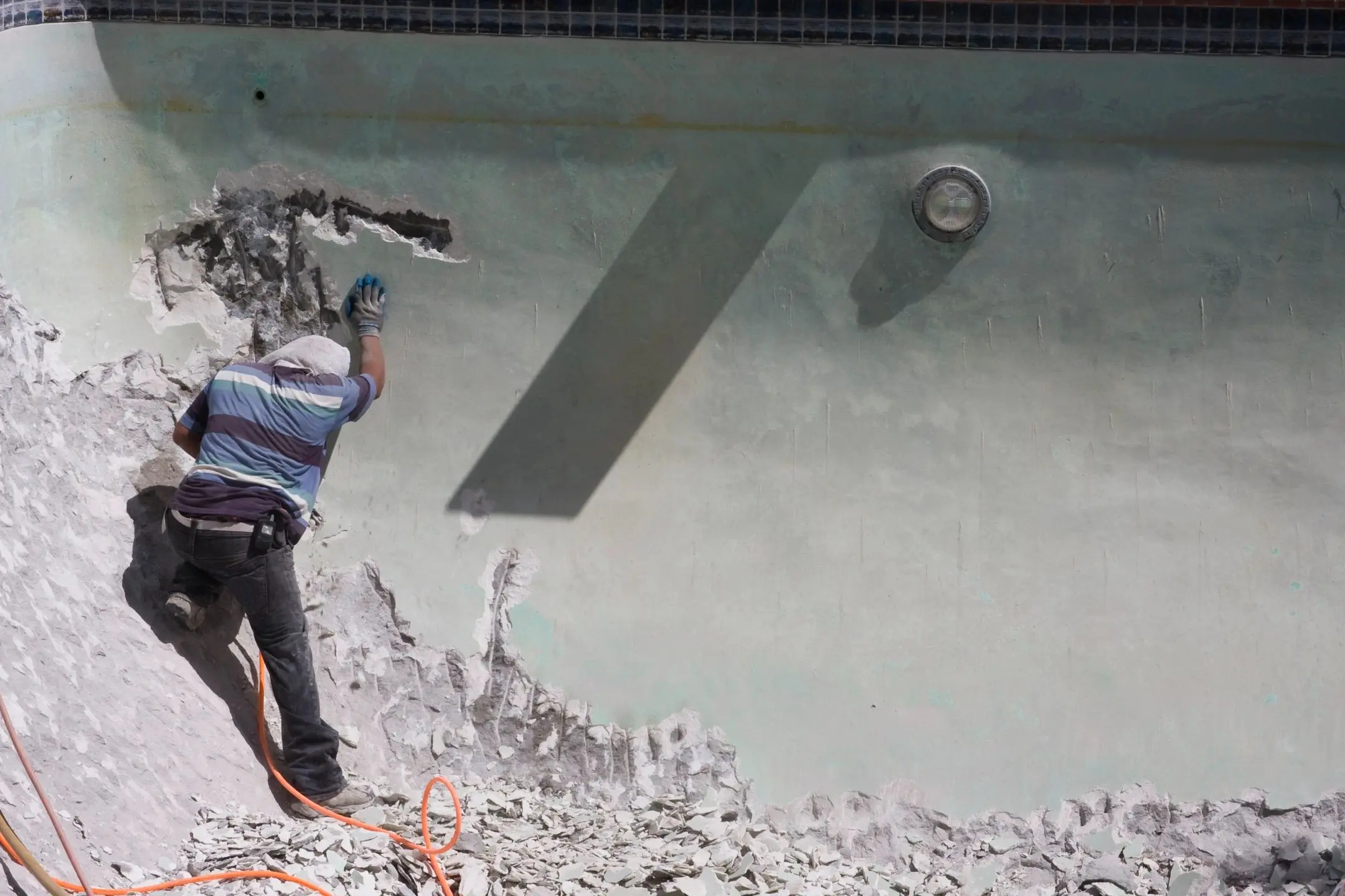 Worker chipping away concrete wall with a power tool.