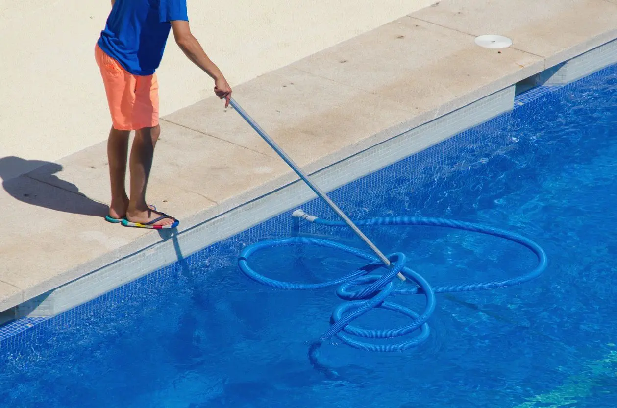 Person cleaning a pool with a long-handled pool vacuum.